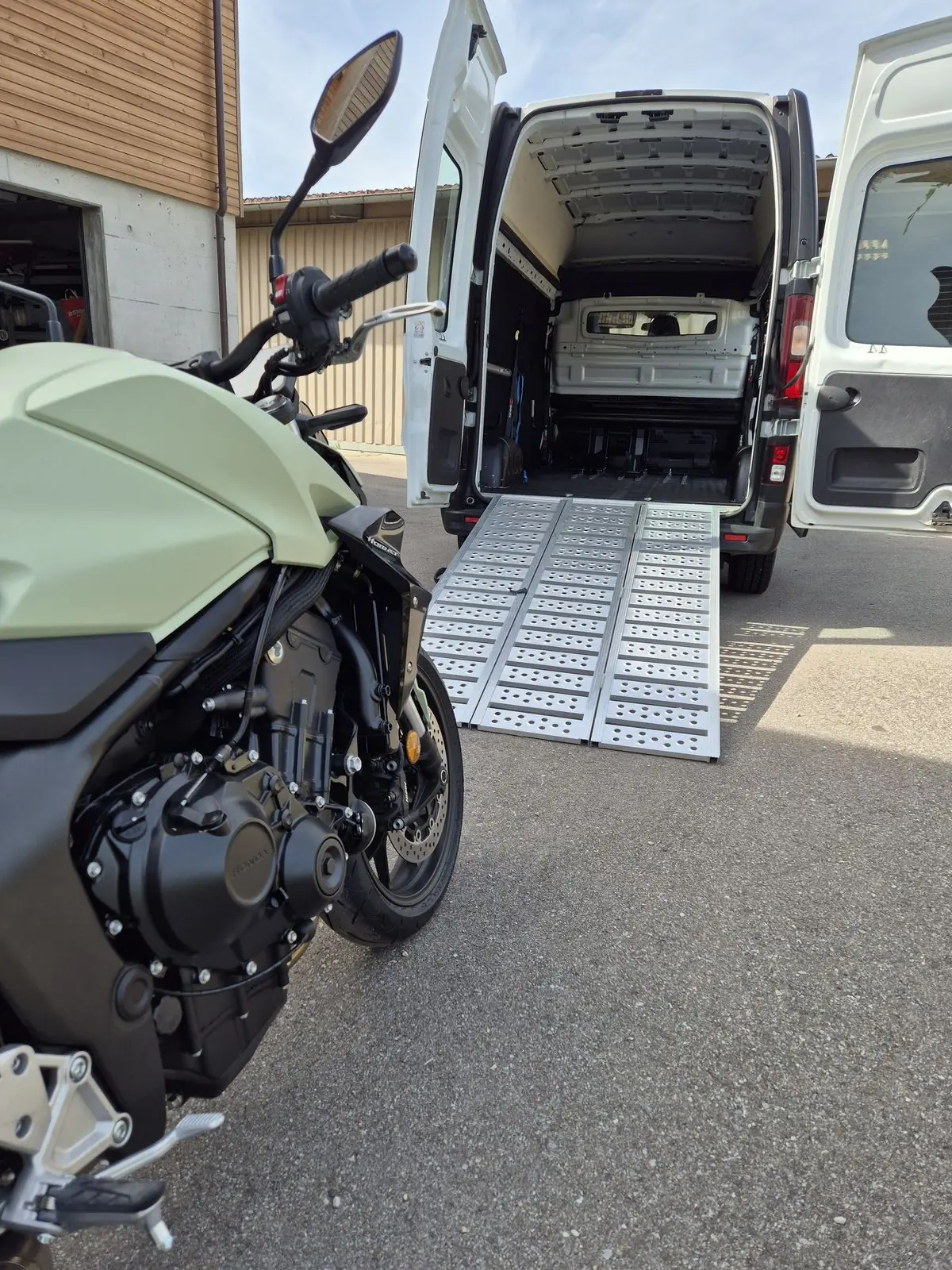 Motorrad vor dem Transporter mit geöffneten Hecktüren und ausgelegter Laderampe